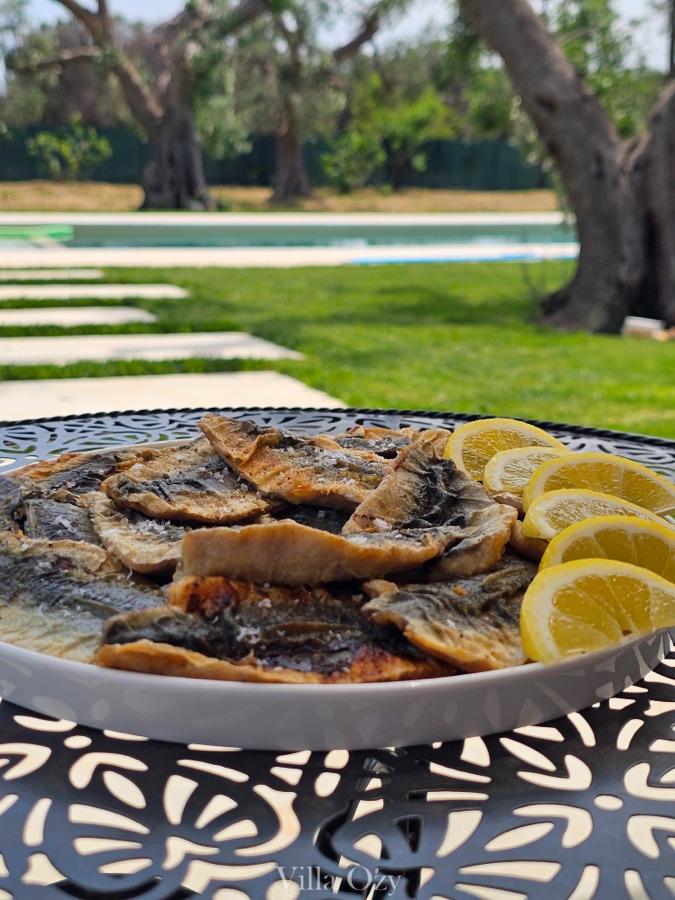 Plate of grilled fish and lemon on a wrought-iron table beside the pool